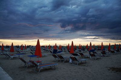 Deck chairs on beach against sky at sunset