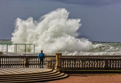 Rear view of man standing by railing against sky