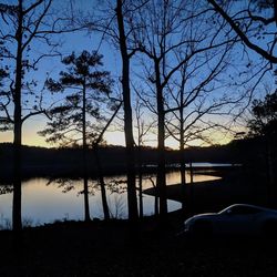 Silhouette trees by lake against sky during sunset