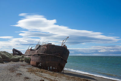 Abandoned ship on beach by sea against sky