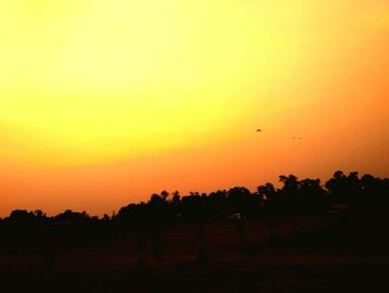 Silhouette birds flying against orange sky