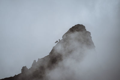 Low angle view of smoke emitting from rock against sky