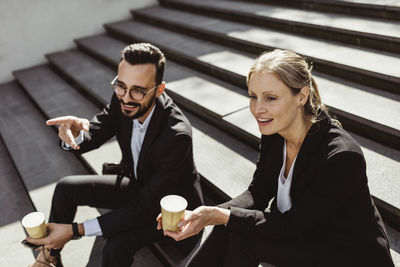 Smiling businessman pointing while sitting with female coworker on staircase