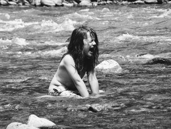 Side view of young long haired boy sitting in a river