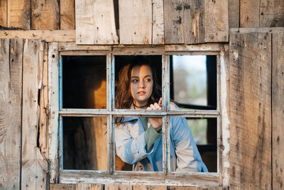Girl looks out the window from an old wooden house, sunlight