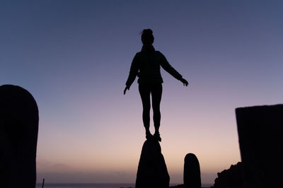 Silhouette man and woman standing against sea at sunset