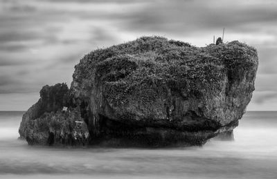 Stack rock in sea against cloudy sky