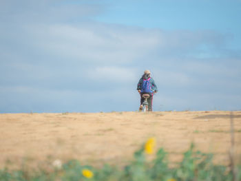 Rear view of woman cycling bicycle on field against sky