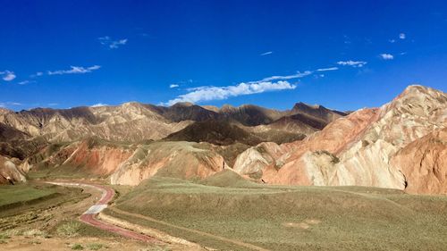 Scenic view of road by mountains against blue sky