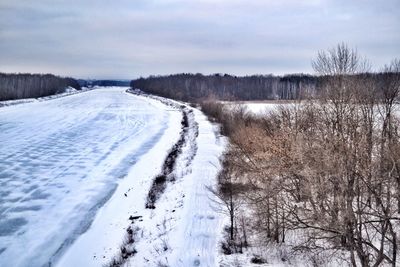 Snow covered road against cloudy sky