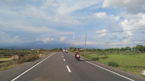 People on highway against cloudy sky