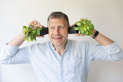 Man covering ears with potted plants against wall