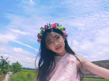 Portrait of beautiful woman with red flower against sky