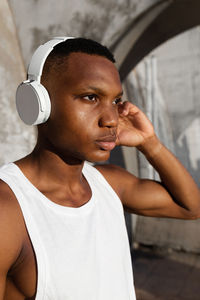 Serious african american male in wireless headphones listening to songs while training outdoors