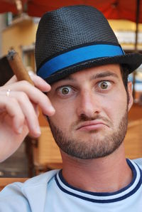 Close-up portrait of young man wearing hat holding cigar