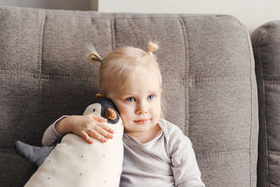 Portrait of a child on a couch with a toy penguin