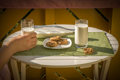 Cropped image of hand holding milk with biscuits in plate on table