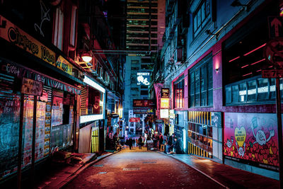 People walking on illuminated street amidst buildings at night