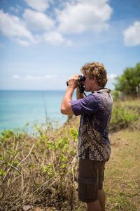 Man looking through binoculars at beach against sky