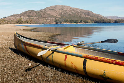 Boat moored on shore by lake against sky