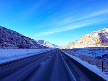 Road amidst snowcapped mountains against clear blue sky