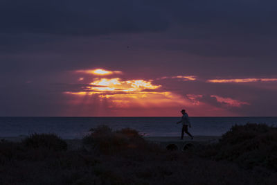 Silhouette person standing on beach against sky during sunset