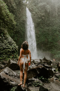 Rear view of woman standing against waterfall