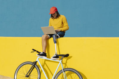 Man with artificial limb and foot working on laptop while sitting on multi colored wall