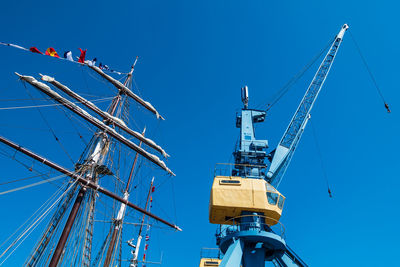 Low angle view of mast by crane against clear blue sky