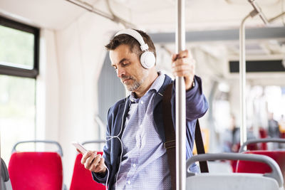 Businessman with smartphone and headphones travelling by bus