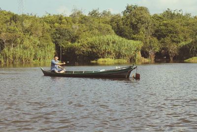 Man sitting in boat on lake against trees