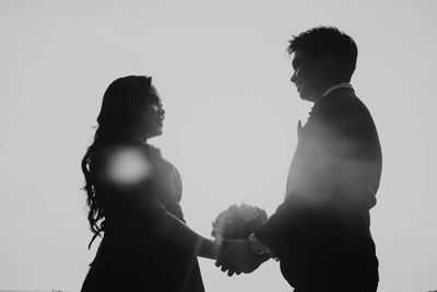 Side view of couple standing against clear sky