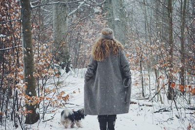 Rear view of woman with dog in forest during winter