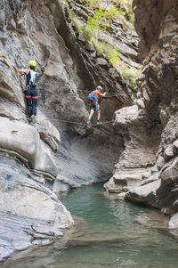 Hikers on rope over stream amidst mountains