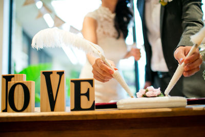 Close-up of newlywed couple signing the document with love text on table