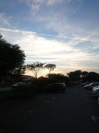 Cars parked on street in city against sky at sunset