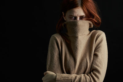 Portrait of young woman standing against black background