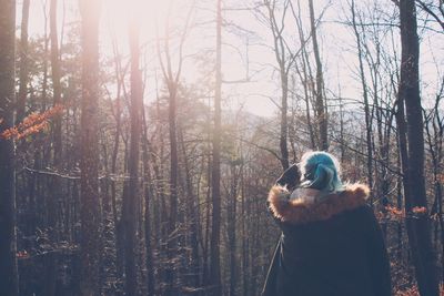 Rear view of man standing by bare trees in forest