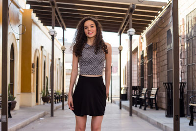 Smiling woman looking away while standing on footpath amidst buildings