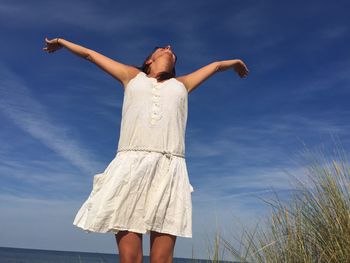 Low angle view of young woman standing with arms outstretched against sky