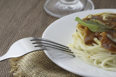 Spagetti bolognese with green basil. silver fork placed next to the white plate