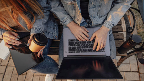 Close-up of hands of man and woman with laptop and tablet while working on laptop on bench in park