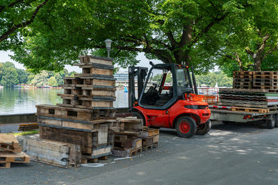 Forklift moving wooden pallets near a lakeside park