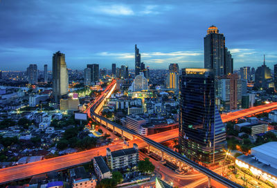 Illuminated road amidst buildings in city against sky at dusk