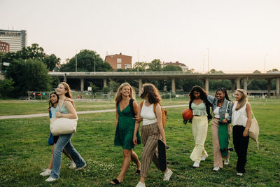 Smiling teenage girls talking with each other while walking in park at sunset