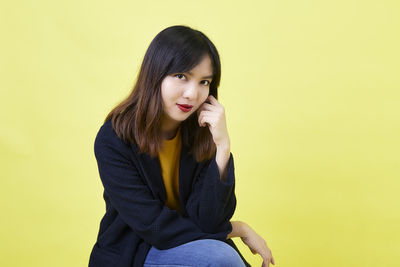Portrait of smiling young woman against yellow background