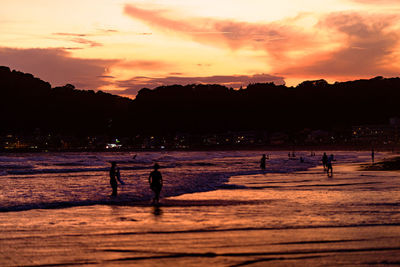 Silhouette people on beach against sky during sunset