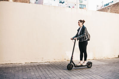 Young woman looking away on footpath against wall