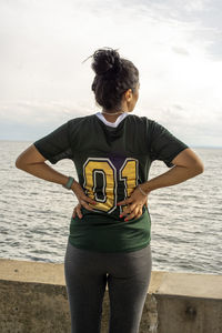 Rear view of woman standing at beach against sky