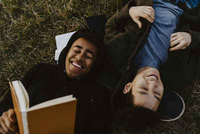 Happy man with diary lying down by male friend on grass in park